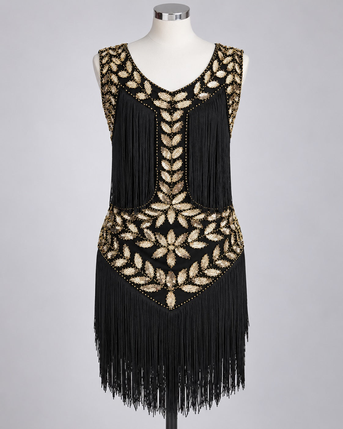 A sleeveless black flapper-style dress with extensive gold beaded leaf and floral patterns and long fringe, displayed on a white mannequin against a light gray studio background.