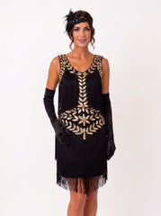 A woman modeling a black 1920s-style flapper dress with gold sequin and bead embellishments, black long gloves, a black feathered headband, and a headpiece against a plain white studio background.