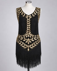 A sleeveless black flapper-style dress with extensive gold beaded leaf and floral patterns and long fringe, displayed on a white mannequin against a light gray studio background.