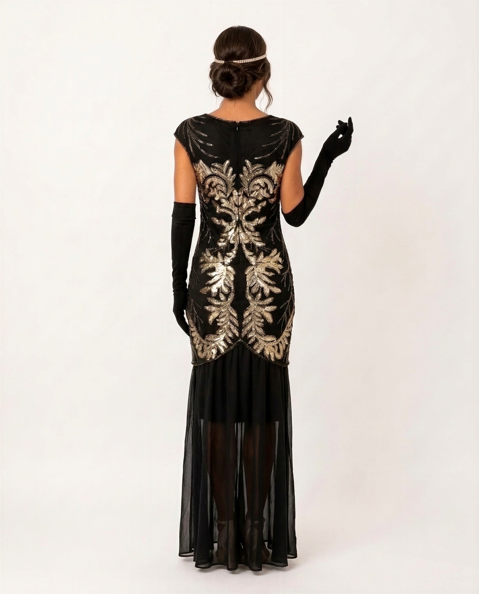 A woman shown from the back wearing a black flapper-style dress with ornate gold sequin embroidery, long black gloves, and black tights against a plain light background.