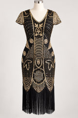 A black 1920s-style flapper dress with elaborate gold beaded and sequined Art Deco patterns, short sleeves, a V-neckline, and a long black fringe hem, displayed on a mannequin against a light gray background.