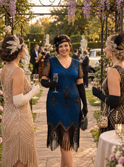 A woman in a 1920s-style blue beaded flapper dress stands in an outdoor garden walkway, smiling and holding a champagne flute, flanked by two other women in elegant flapper dresses.
