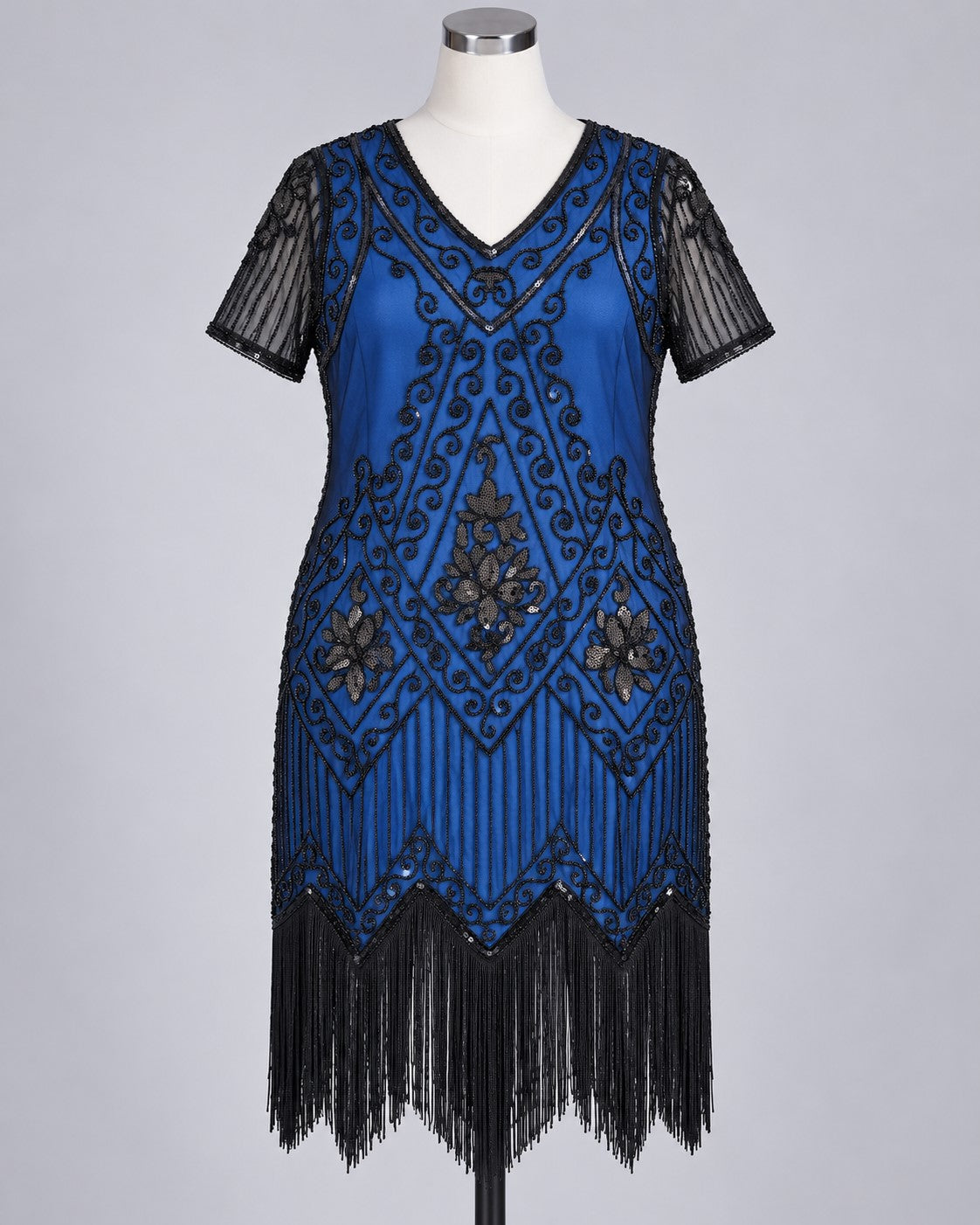A blue 1920s flapper-style dress with black sequin embroidery, fringe, and sheer black short sleeves, displayed on a mannequin against a light gray background.