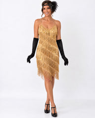 A woman modeling a gold 1920s-style fringe dress with black gothic-style accessories, including long black gloves, a black feathered headband, and black Mary Jane heels, against a plain white studio background.