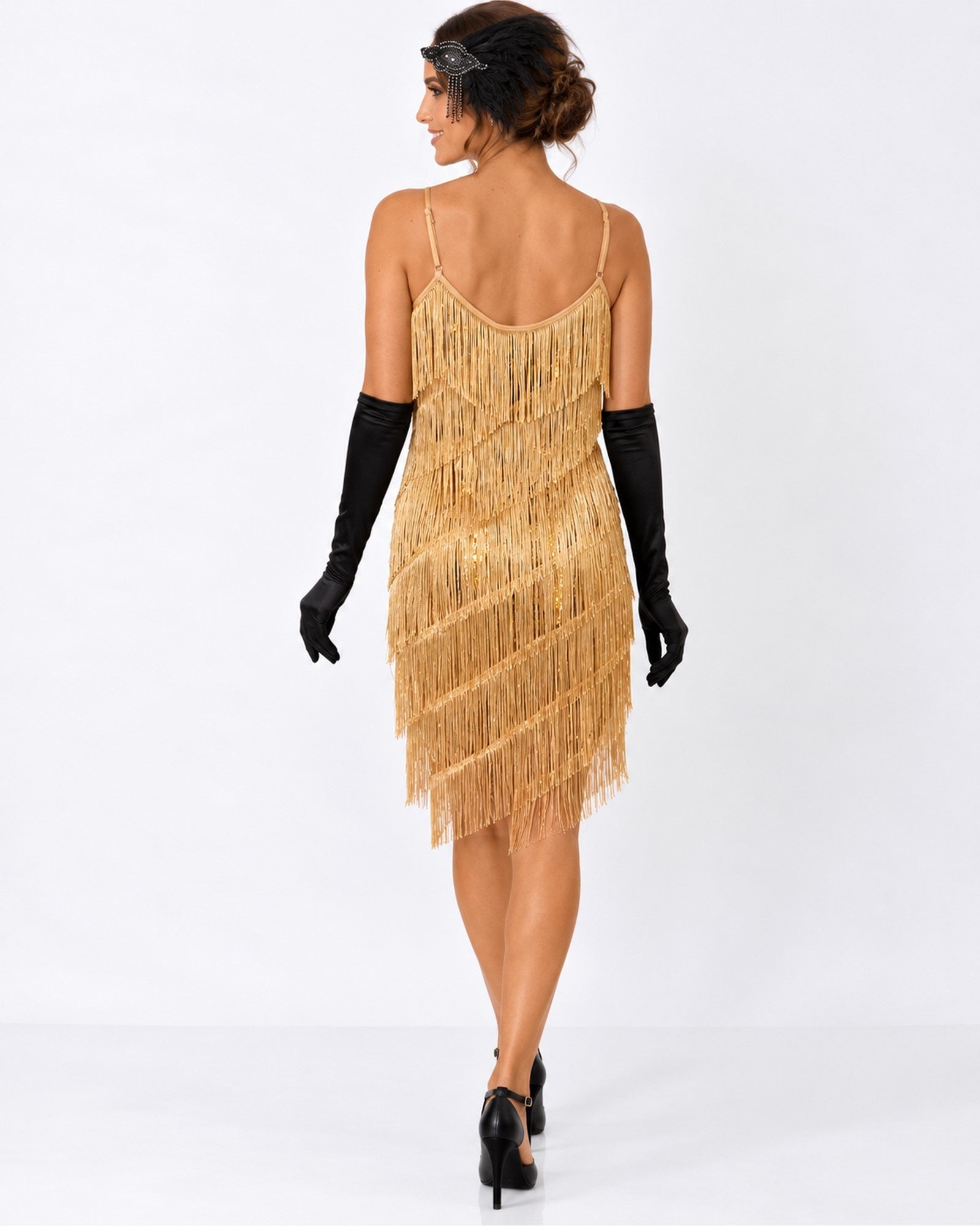 A woman shown from the back wearing a old fringe & sequin 1920s flapper dress with black opera gloves and black heels, standing against a plain white studio background.