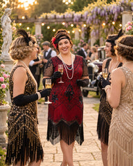 Three women in 1920s flapper-style dresses converse outdoors at a garden party. The center woman wears a dark red and black fringed dress with black gloves and pearl necklaces, while the others wear black and beige embellished dresses.
