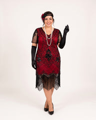 A plus size woman modeling a 1920s-style flapper dress in deep red and black, featuring black lace sleeves, black gloves, a black headband with a red flower, and a long pearl necklace, against a plain white studio background.
