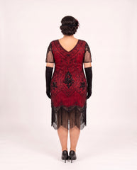 A woman viewed from the back wearing a red and black plus size 1920s-style flapper dress with black gloves and black heels, standing against a plain light background.