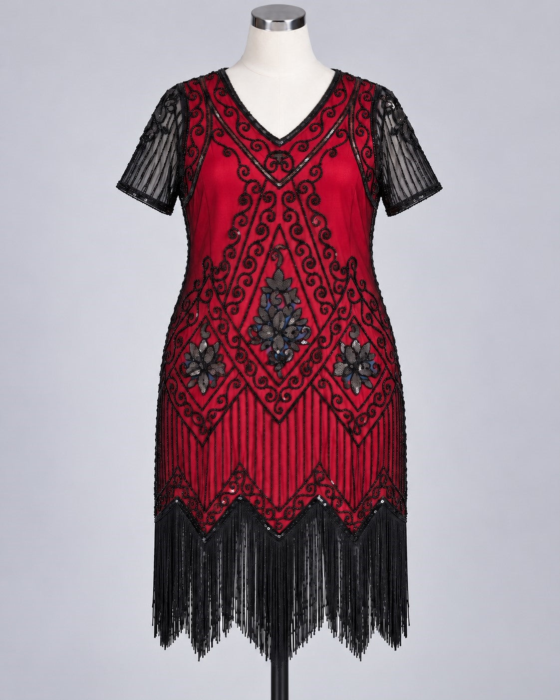 A red and black 1920s-style flapper dress displayed on a mannequin against a light gray studio background. The dress features black sequin fringe, black embroidered scrollwork, and sheer black short sleeves.