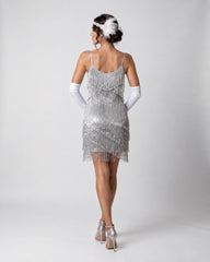 A woman shown from the back wearing a silver sequined fringe dress, white opera gloves, and silver high heels against a light gray studio background.