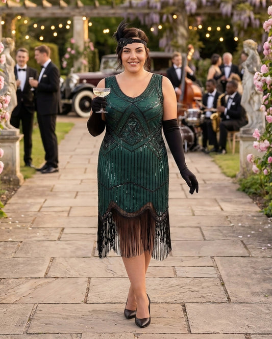 A woman in a 1920s-style green plus size flapper dress with black fringe, long black gloves, and a headband walks down a stone path at an outdoor event, holding a glass of white wine.